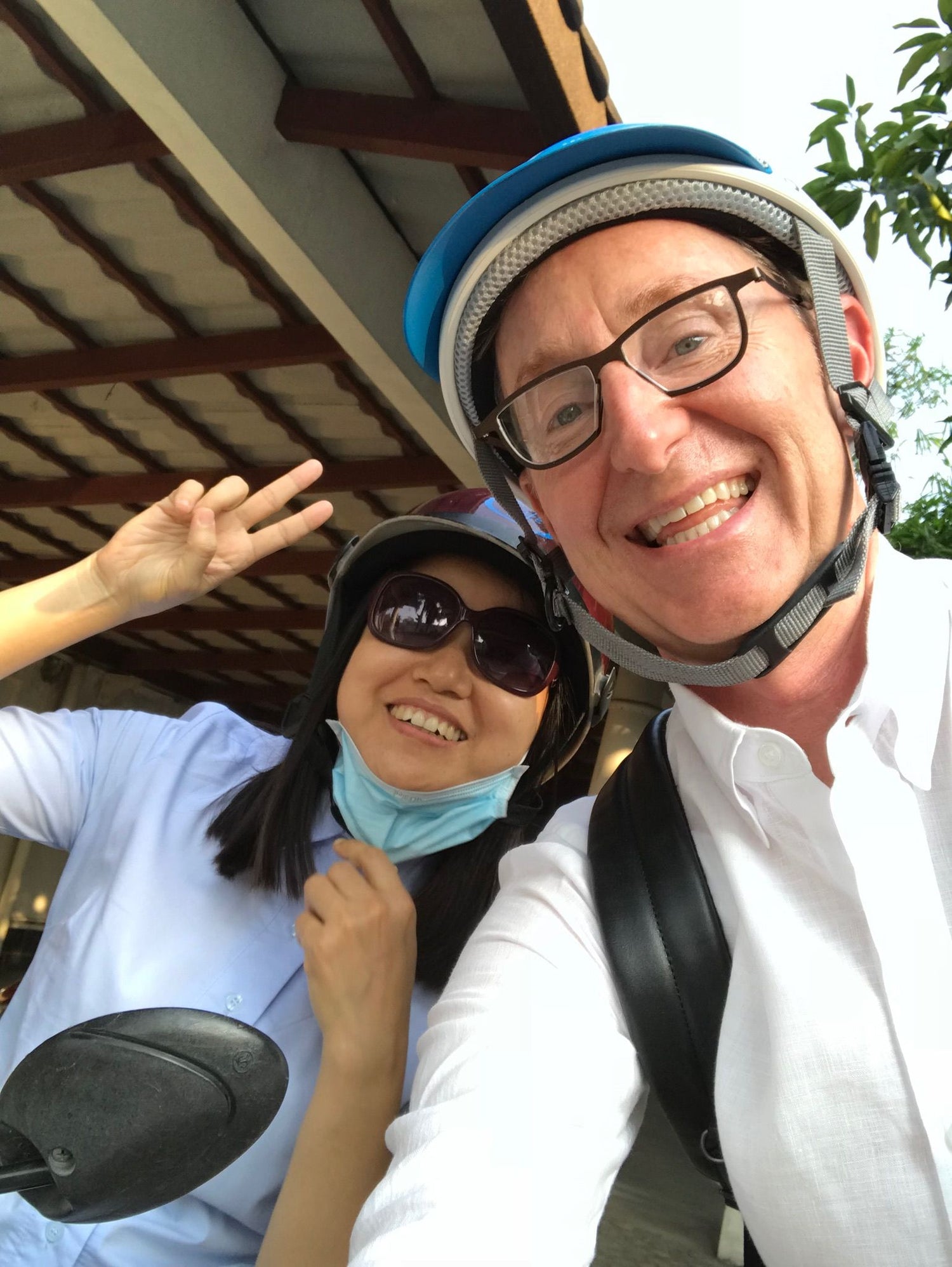 Two people in helmets smiling and posing for a selfie, one holding up a peace sign