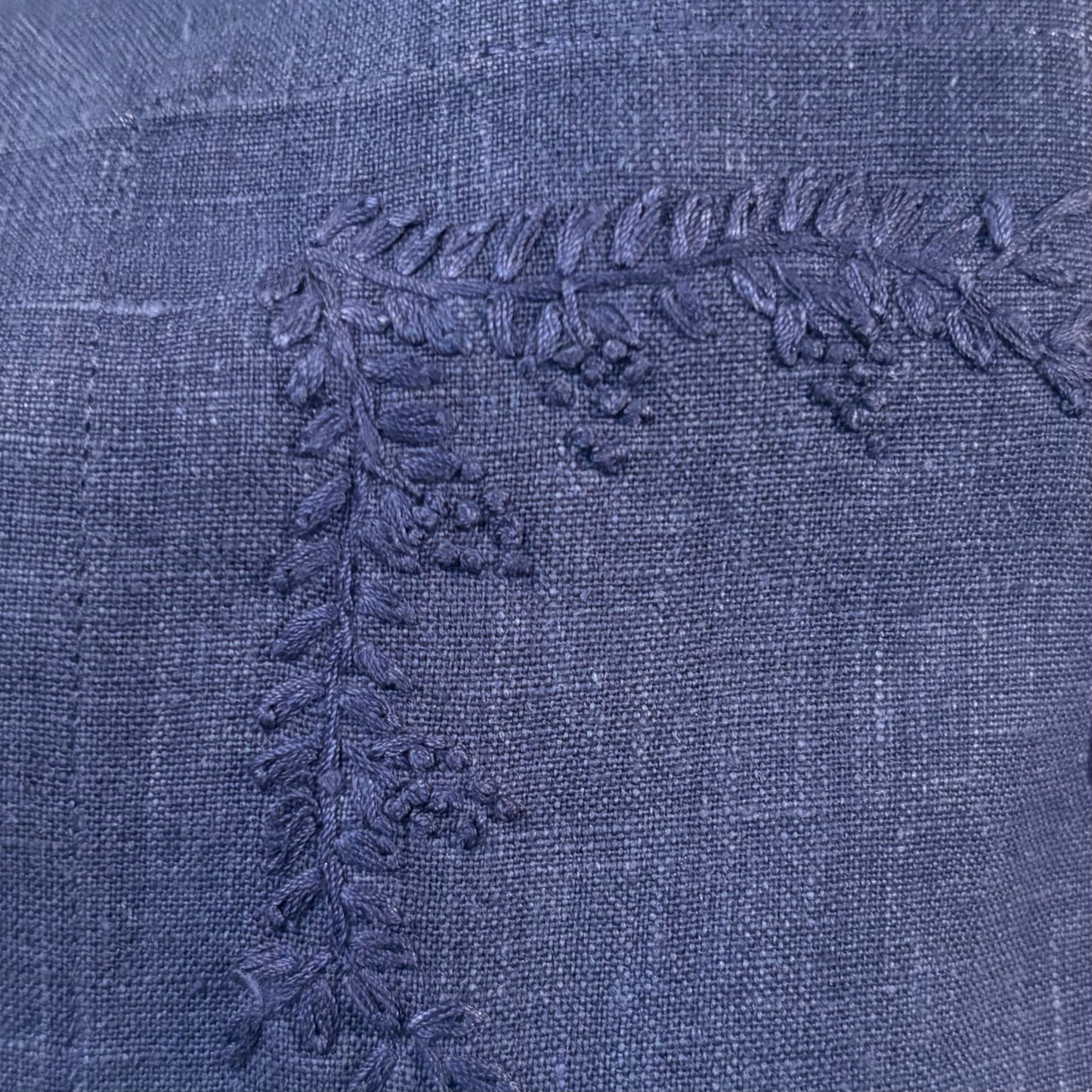Close-up of blue linen with a raised embroidered leafy branch and small berry clusters.