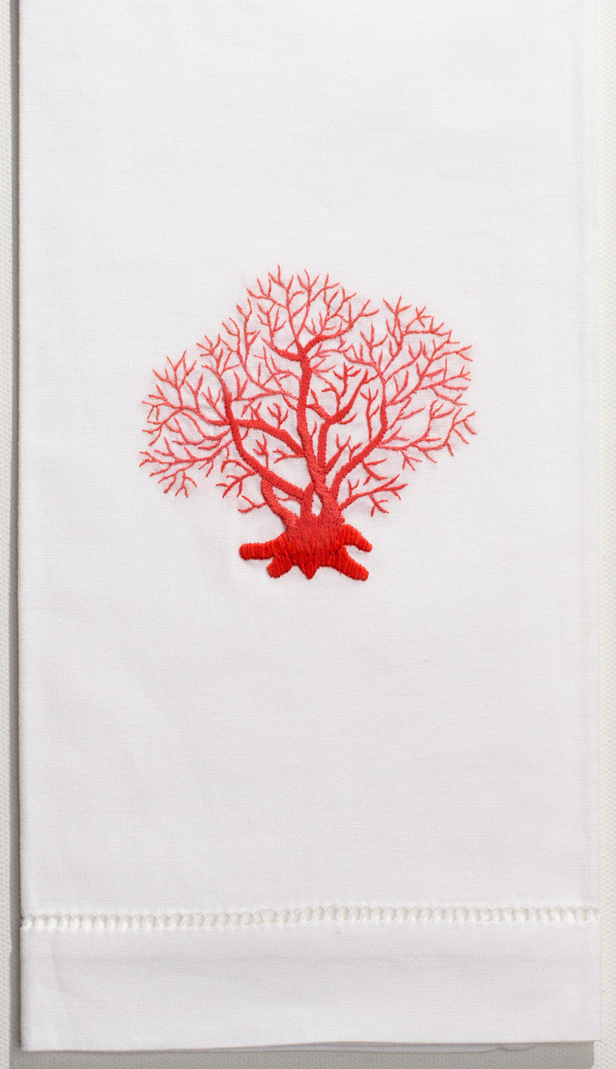 A white hand towel with a hemstitch. A piece of red coral is embroidered in the center.