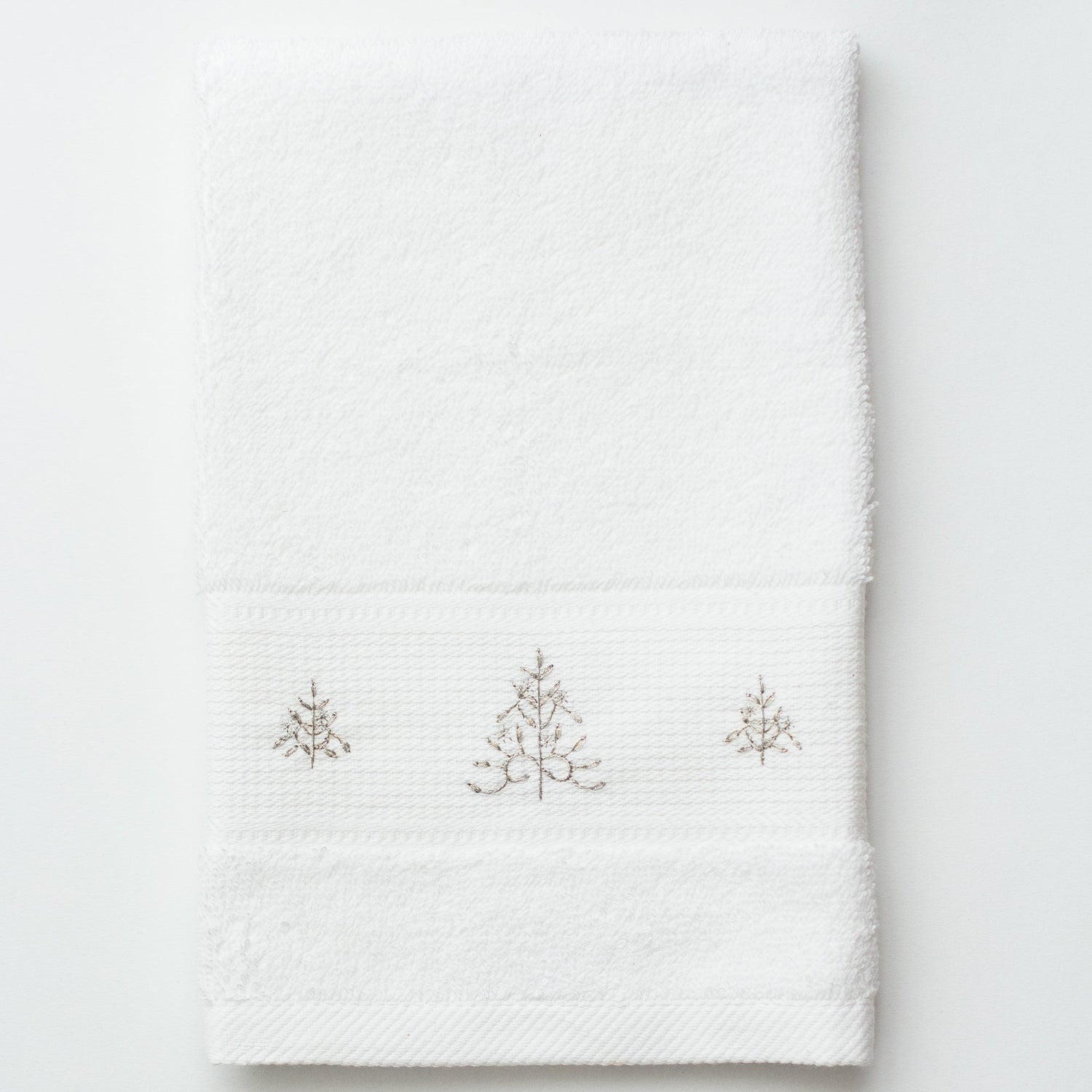 A white terry towel. 3 glittering silver christmas trees are embroiderevd in the center
