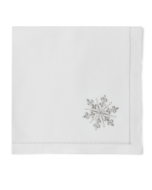 A white napkin with a hemstitch. A silver snowflake is embroidered in the bottom right corner
