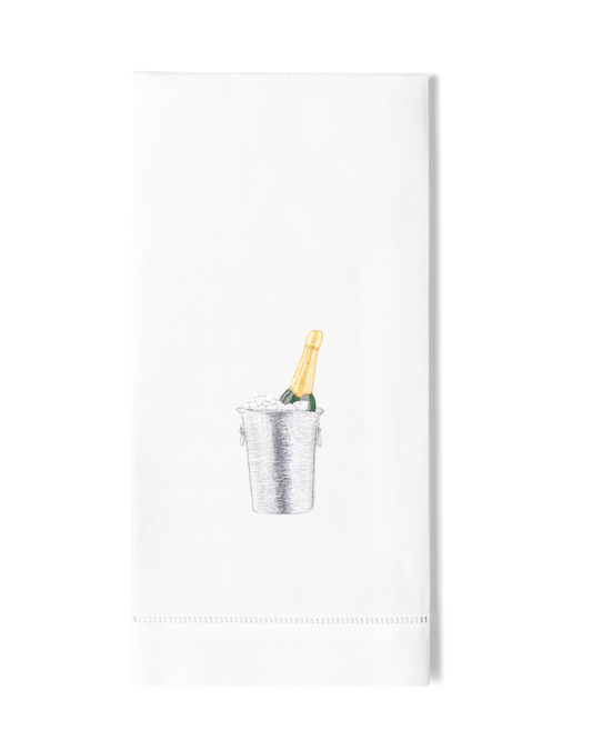 A white hand towel with a hemstitch. A champagne bottle in a silver ice bucket is embroidered in the center.