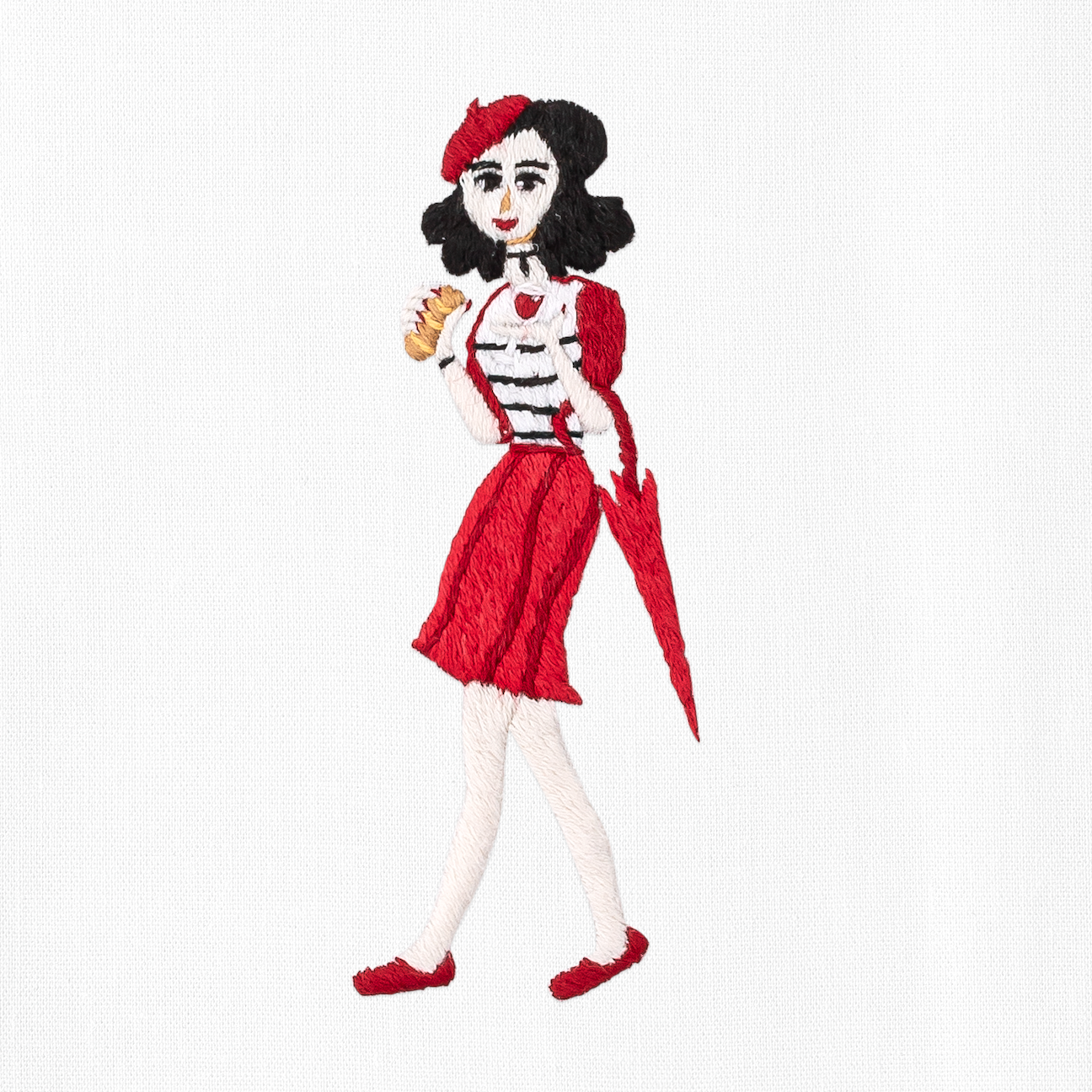 A close up detailed image of the embroidery - A woman in red dress and hat holding a pastry and an umbrella.