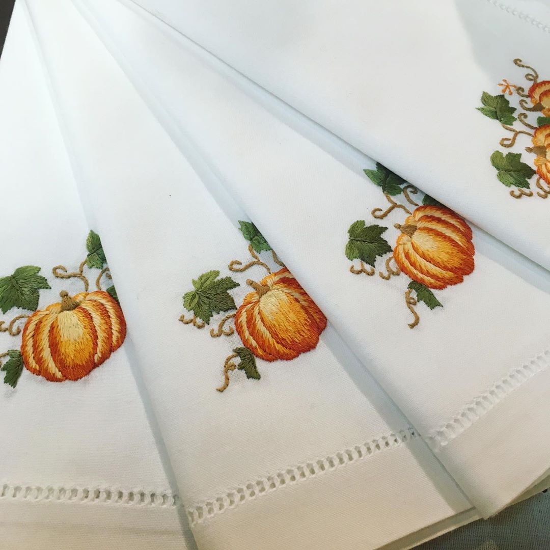 White napkins with embroidered orange pumpkins and green leaves fanned out side by side