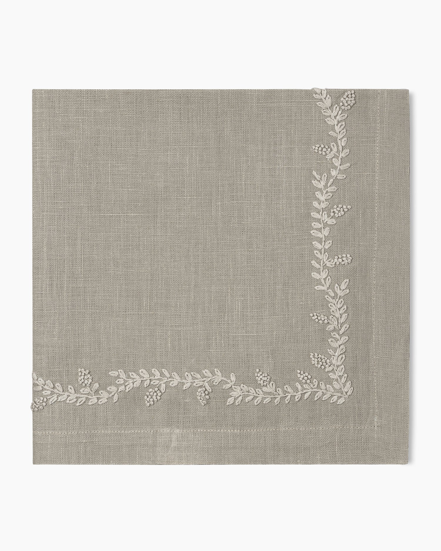A beige Prism Vine Linen Dinner Napkin - 13 Colors with white embroidered leaves, perfect for table linens.