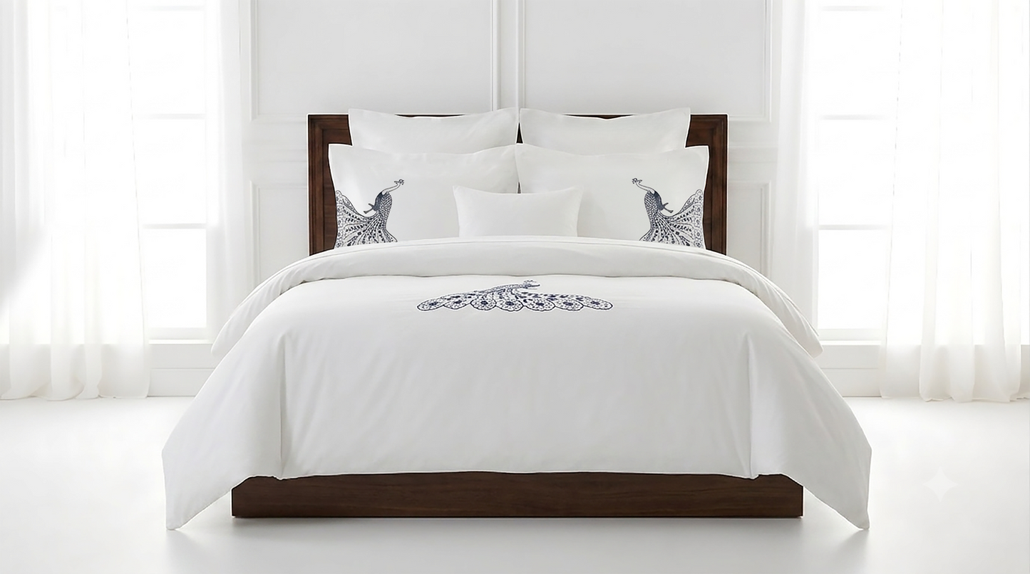 A white comforter set on a dark wood bed frame, styled with multiple white pillows, including two decorative pillows featuring a blue and gray bird design, set against a bright white window background.