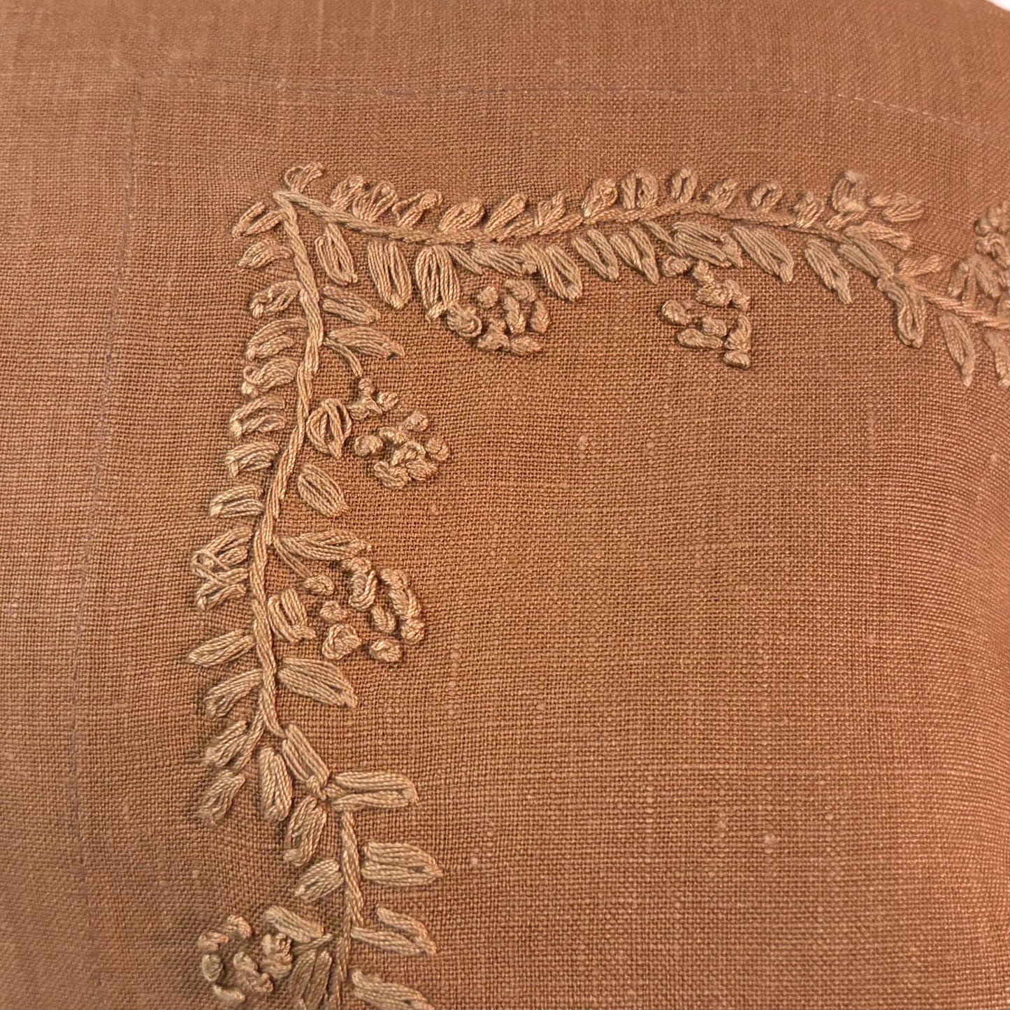 Close-up of a textured terracotta linen fabric with a corner embroidered vine and berry design in a matching beige thread.