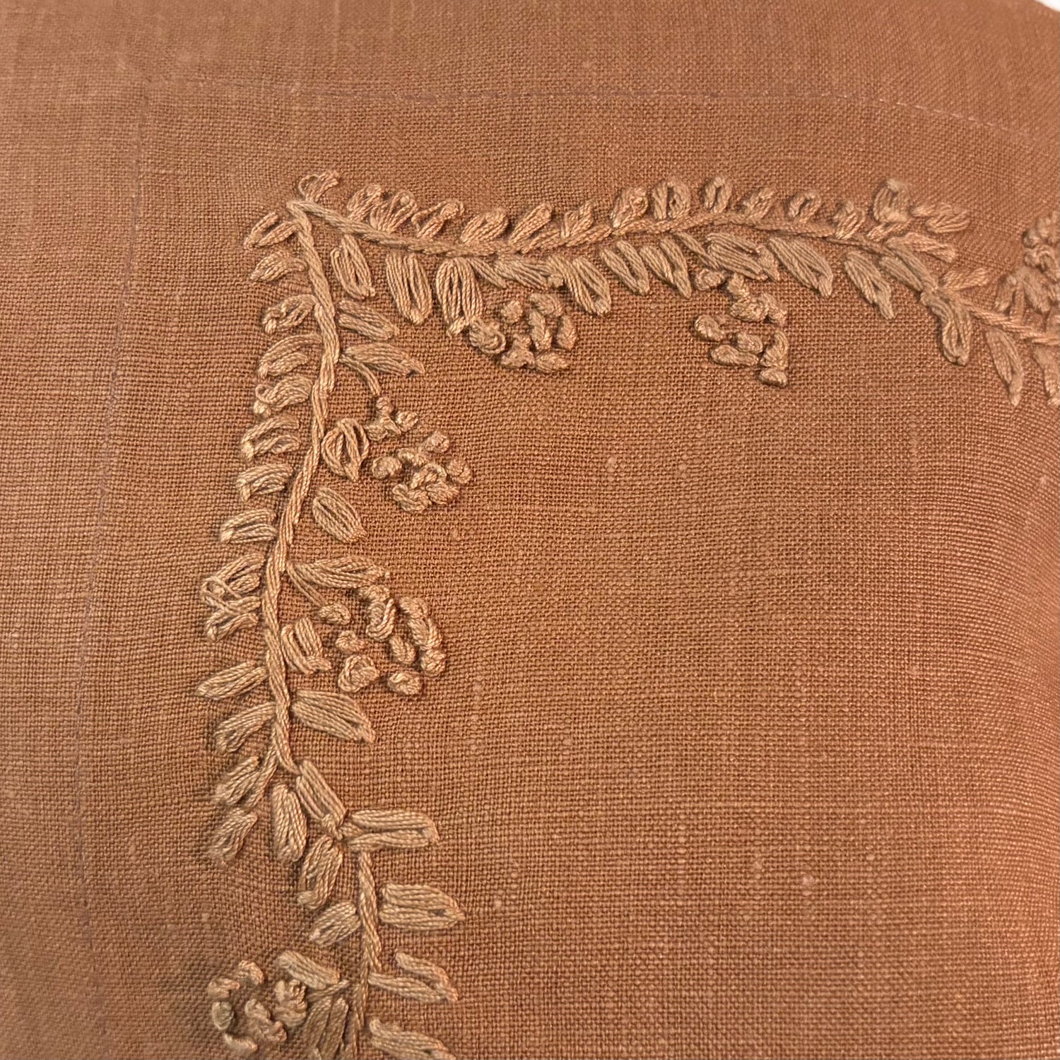 Close-up of a textured terracotta linen fabric with a corner embroidered vine and berry design in a matching beige thread.