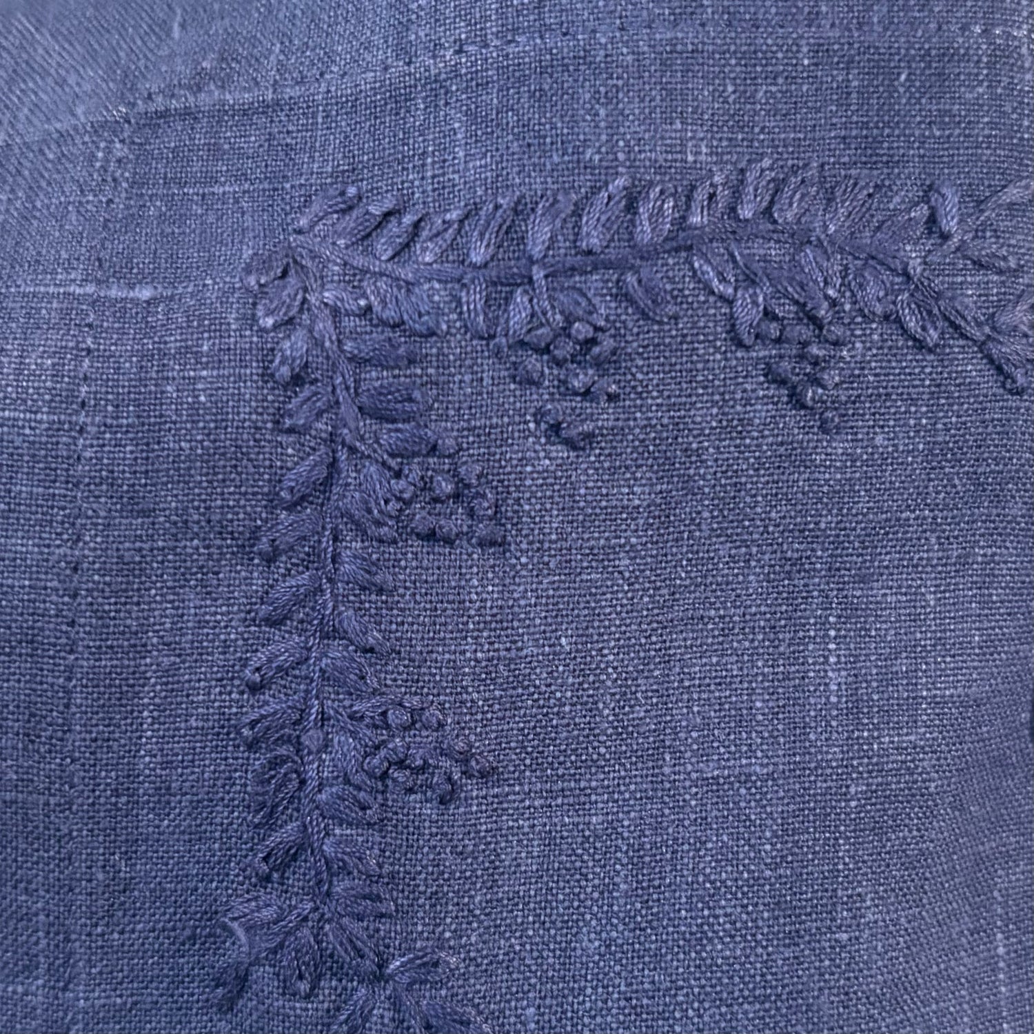 Close-up of blue linen with a raised embroidered leafy branch and small berry clusters.