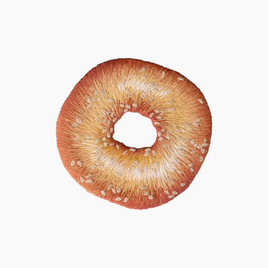 Hand embroidered cotton towel with seeded brown bagel on a white background