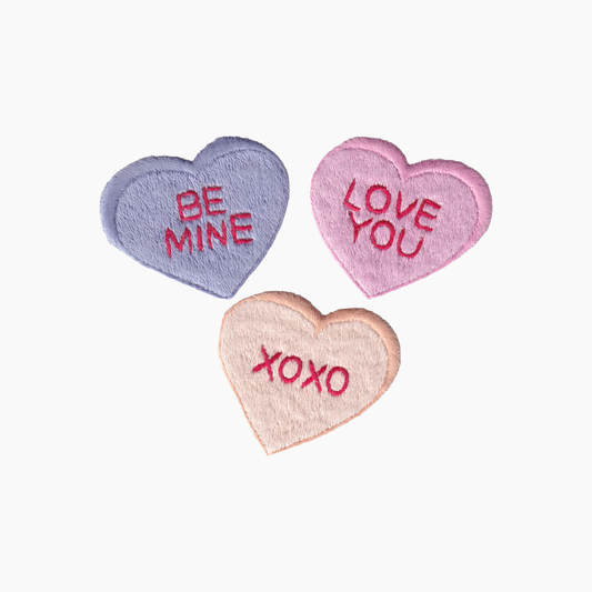 Hand embroidered cotton towel with three heart-shaped candies with 'Be Mine', 'Love You', and 'XOXO' text on a white background