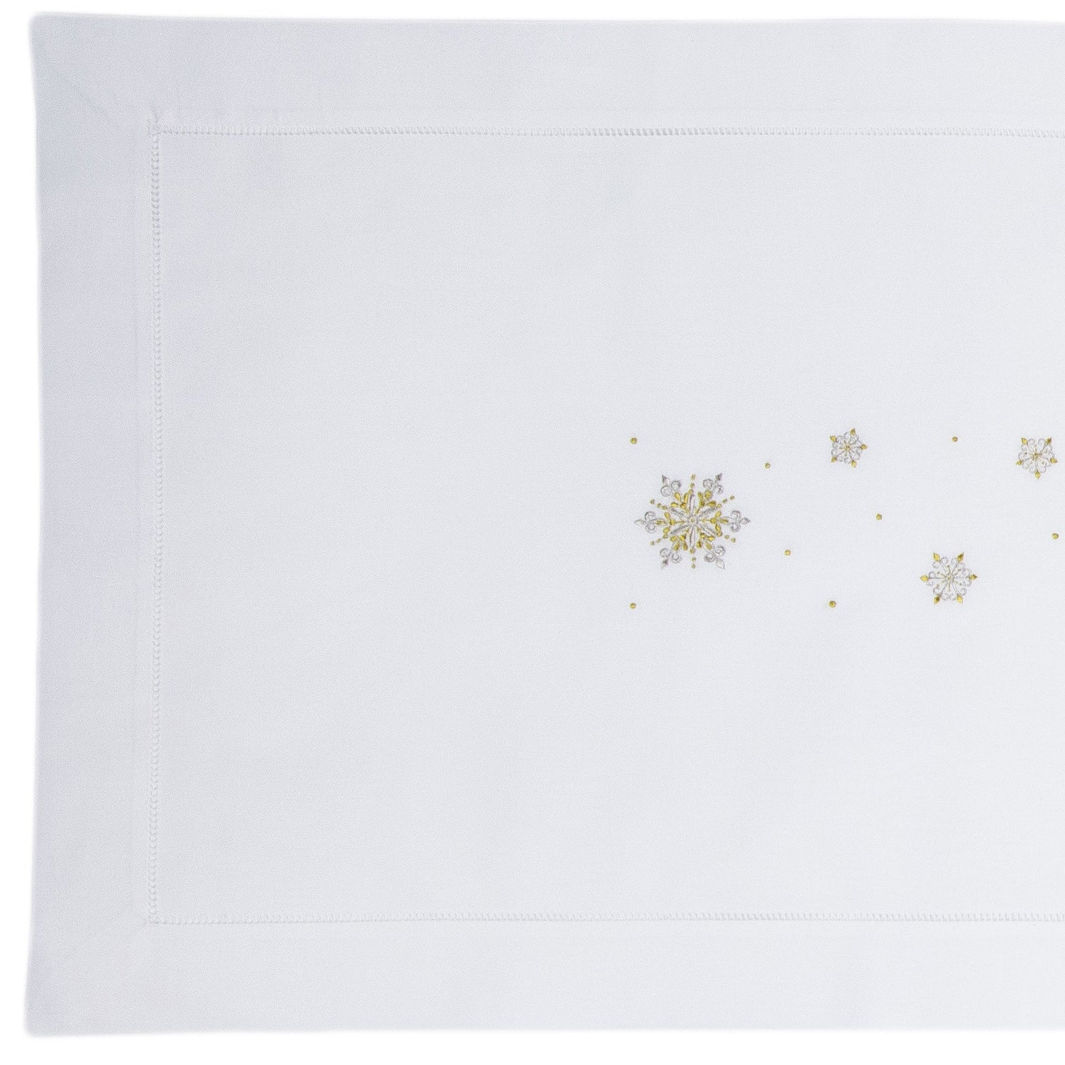 A white table runner with a hemstitch border. Gold & silver metallic snowflakes are embroidered in a line down the middle