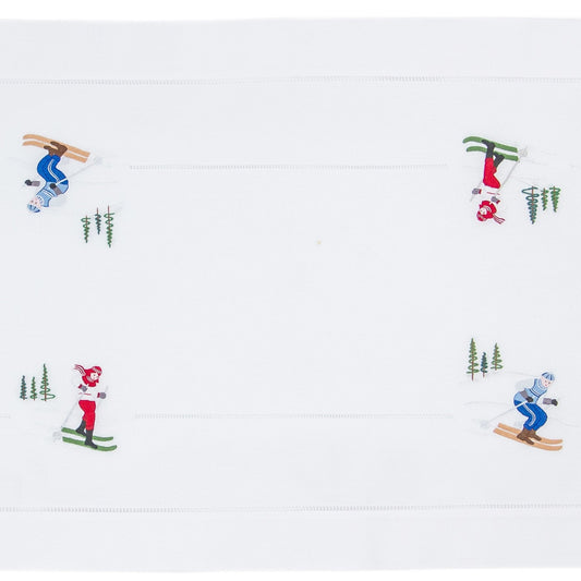 A white table runner with a hemstitch border. Skiers are embroidered in a border around the edge