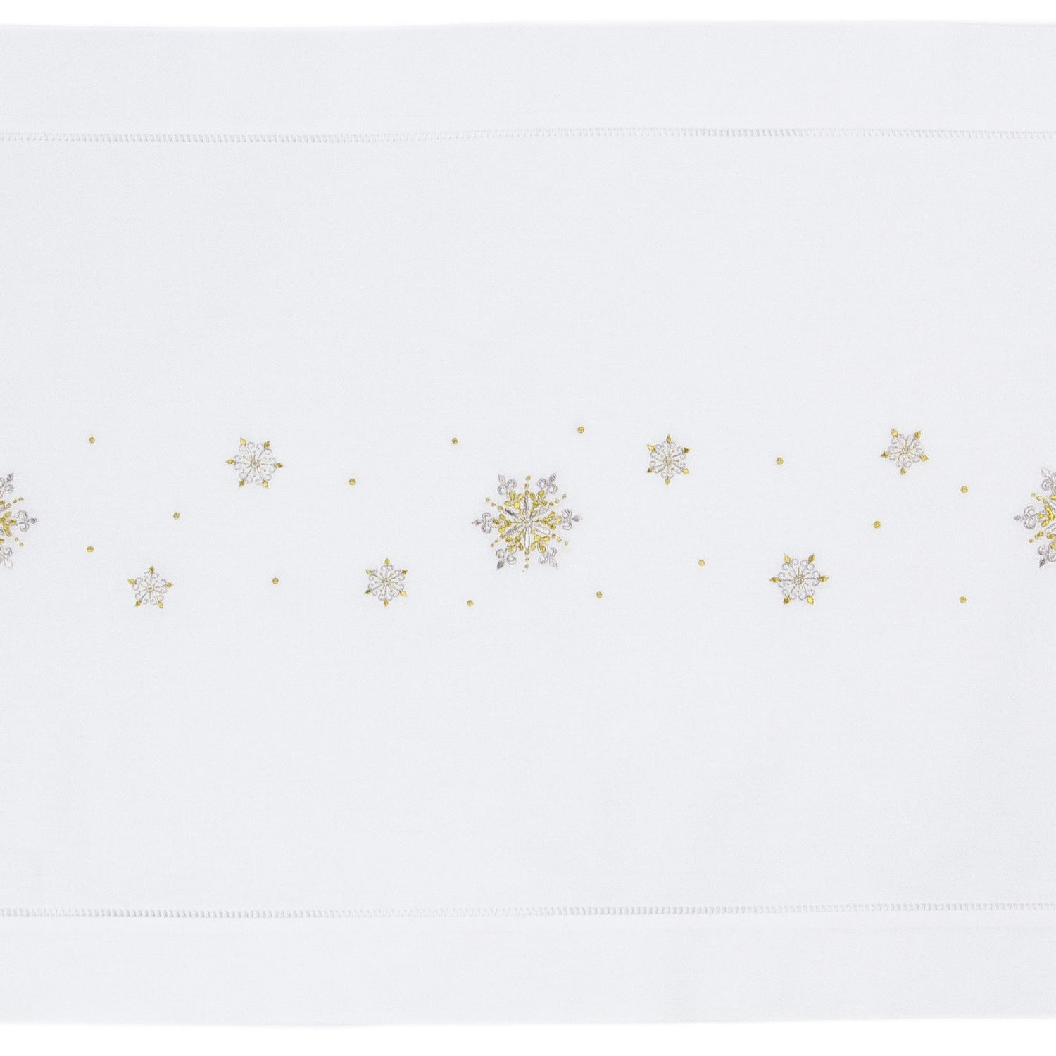 A white table runner with a hemstitch border. Gold & silver metallic snowflakes are embroidered in a line down the middle