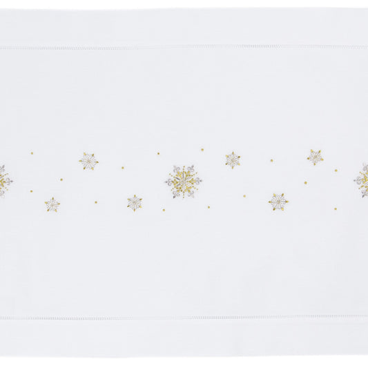 A white table runner with a hemstitch border. Gold & silver metallic snowflakes are embroidered in a line down the middle