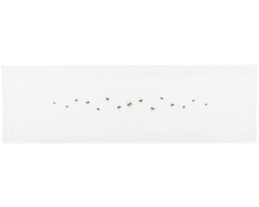A white table runner with a hemstitch border. A line of bumblebees are embroidered scattered in a line down the middle.