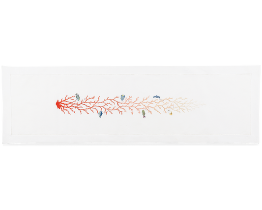A white table runner. A red coral that fades to light pink and many fish are embroidered in a line down the middle.