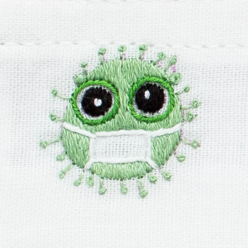 A detailed closeup of the embroidery - a green germ with big eyes and a white facemask on