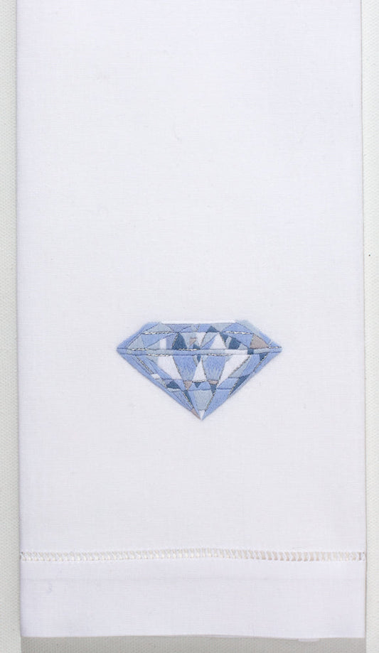 A white hand towel with a hemstitch. A blue and white silvery diamond is embroidered in the center.
