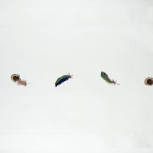 A white runner with a hemstitch border. Embroidered in a line down the center are multiple peacock feathers.