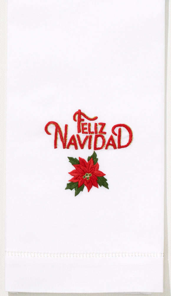 A white hand towel with a hemstitch. Red text saying “Feliz Navidad” above a poinsettia is embroidered in the center.