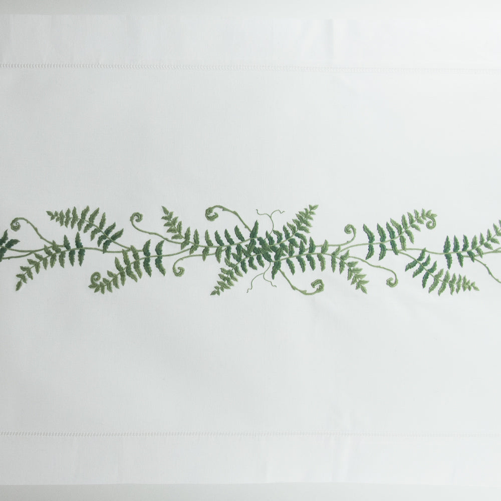 A white runner with a hemstitch border. Curling fern fronds are embroidered in a line down the center.