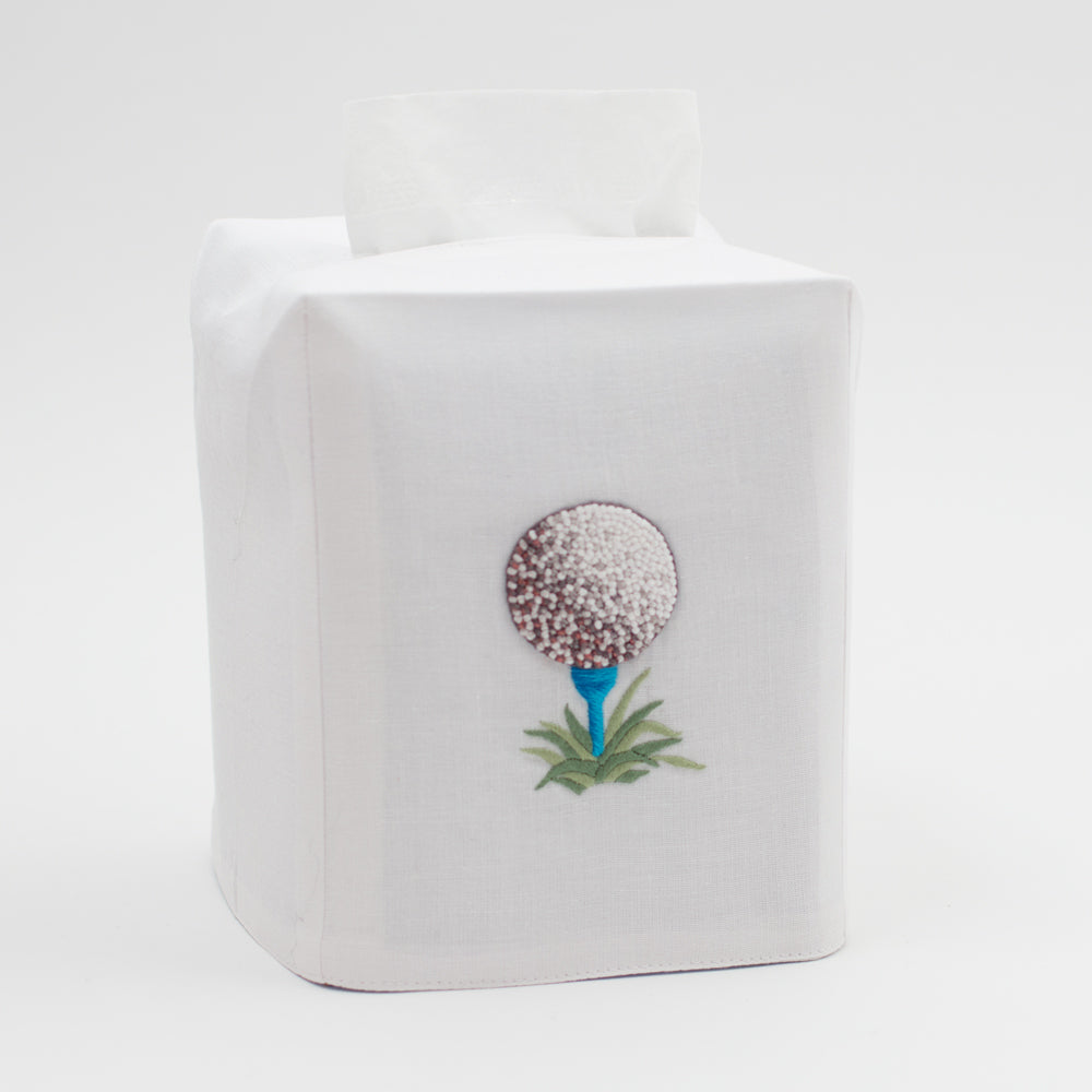 A white tissue cover with a french knotted golf ball on a blue tee on grass in the center.