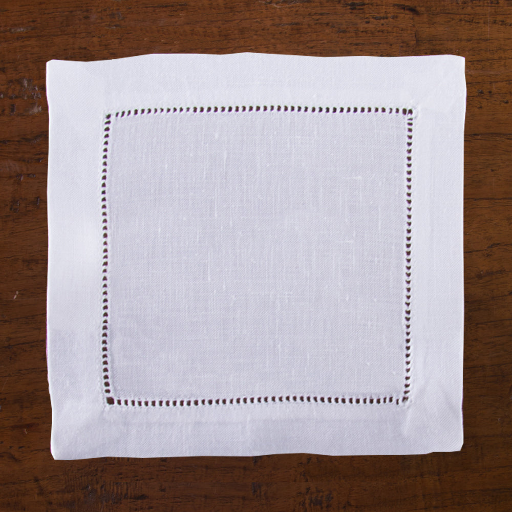 a white linen cocktail napkin with a hemstitch border on a wooden table