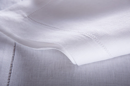 A close-up of a white linen placemat with a hemstitch border.