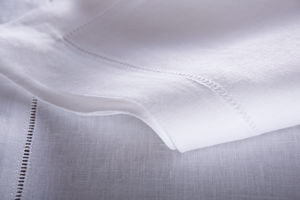 A close up of a white linen tablecloth with a hemstitch border folded over itself.