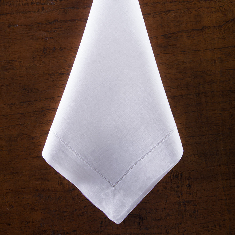 A white linen napkin with a hemstitch border folded on top of a wooden table.