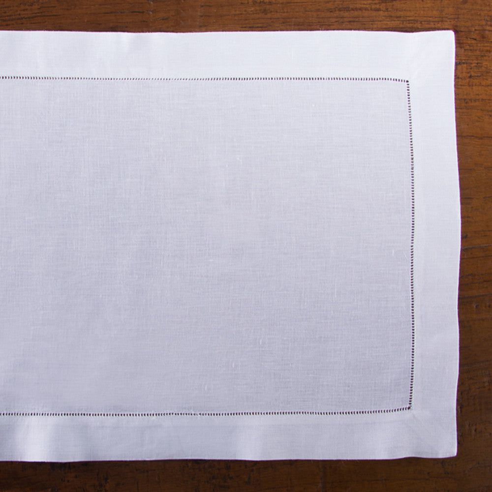A white linen placemat with a hemstitch border placed on a wooden table.