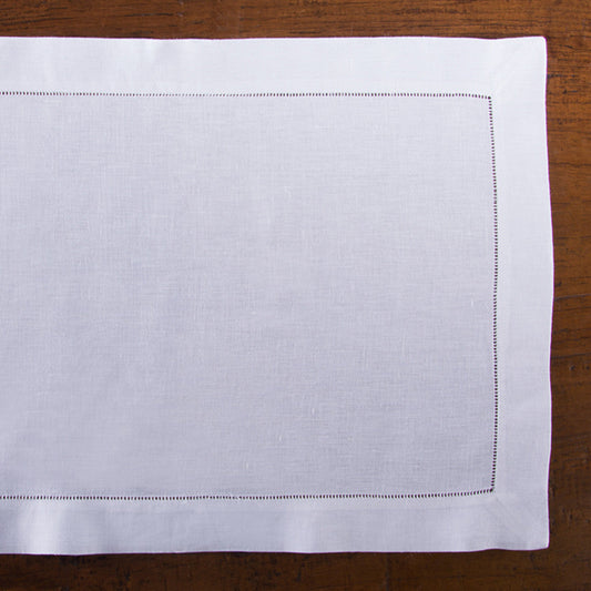 A white linen placemat with a hemstitch border placed on a wooden table.