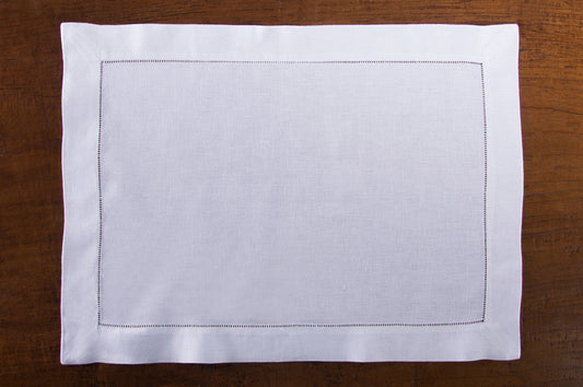 A white linen placemat with a hemstitch border placed on a wooden table.
