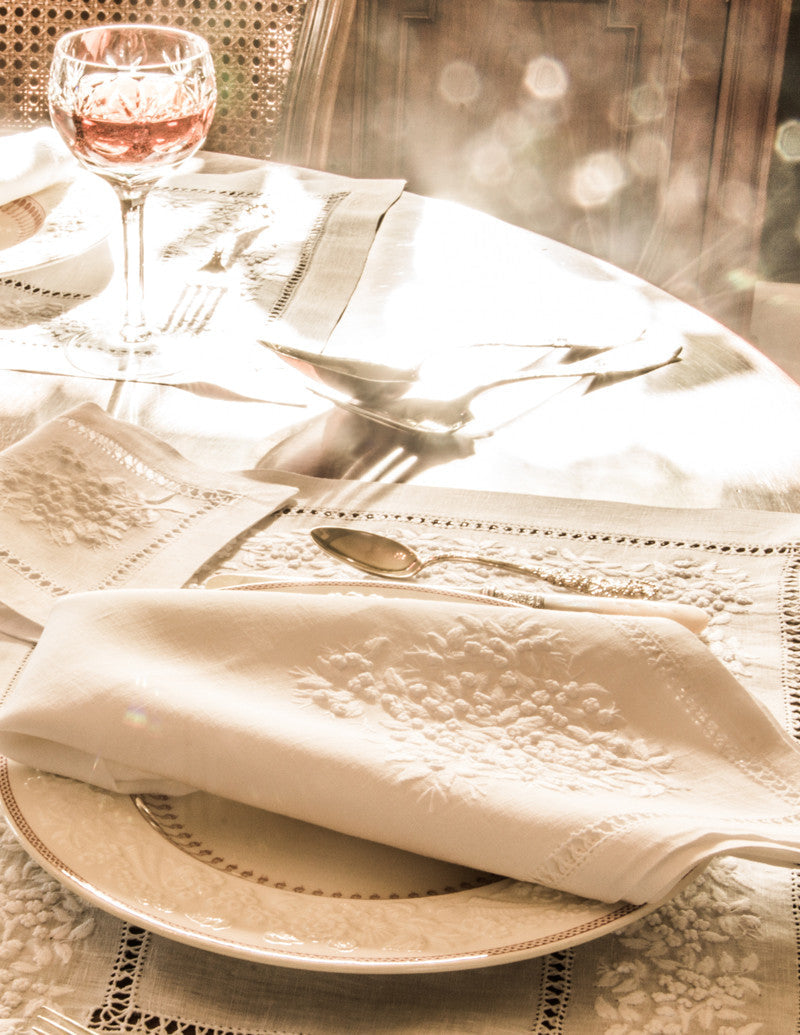 A closeup shot of a single place setting with a white on white placemat, napkin and cocktail napkin