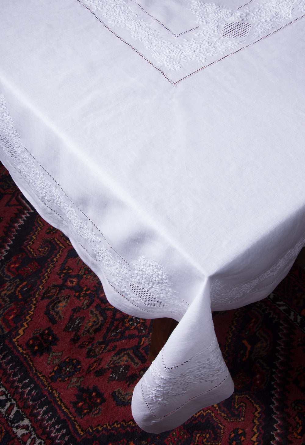 A white linen tablecloth with a hemstitch border and white french knot floral embroidery draped off a table