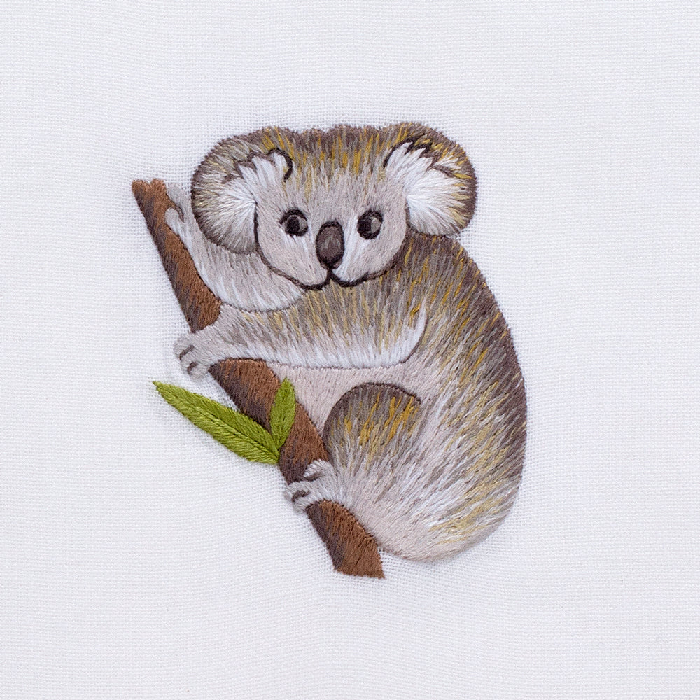 A detailed image of the embroidery - A gray koala climbing a brown branch with two green leaves