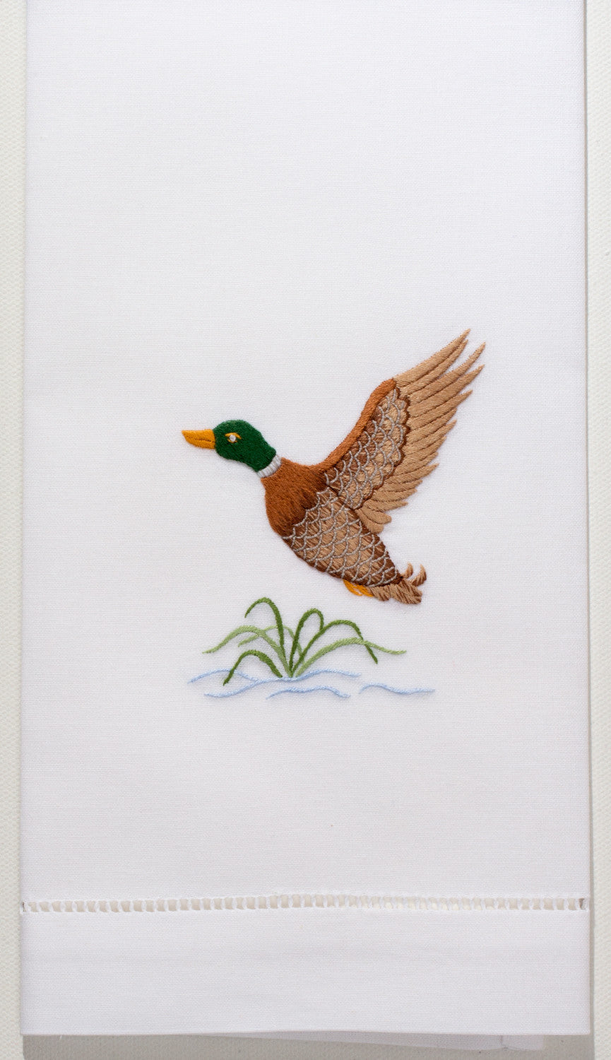 A detailed image of the embroidery -  A mallard flying above a little water with a green plant
