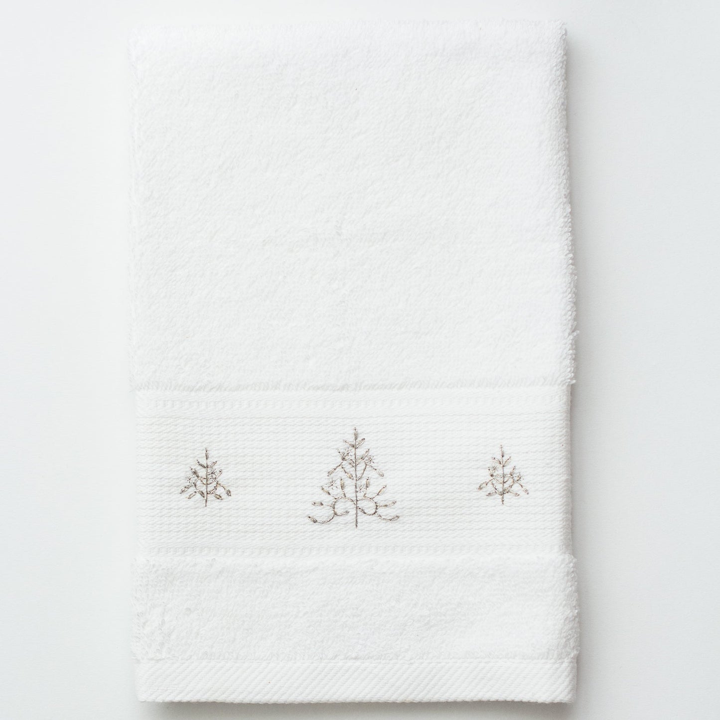 A white terry towel. 3 glittering silver christmas trees are embroiderevd in the center