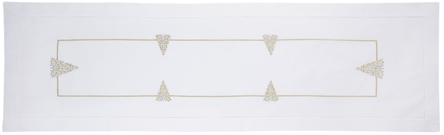 A white table runner with a hemstitch border. Glittering gold and silver christmas trees run down the middle