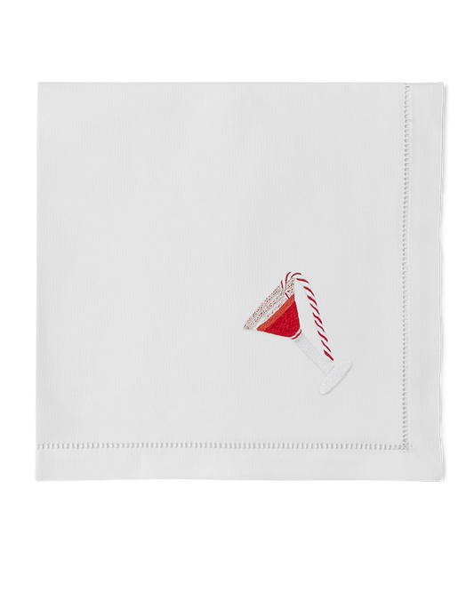 A white napkin with a hemstitch border. A red martini with a candy cane garnish is embroidered in in the bottom right corner