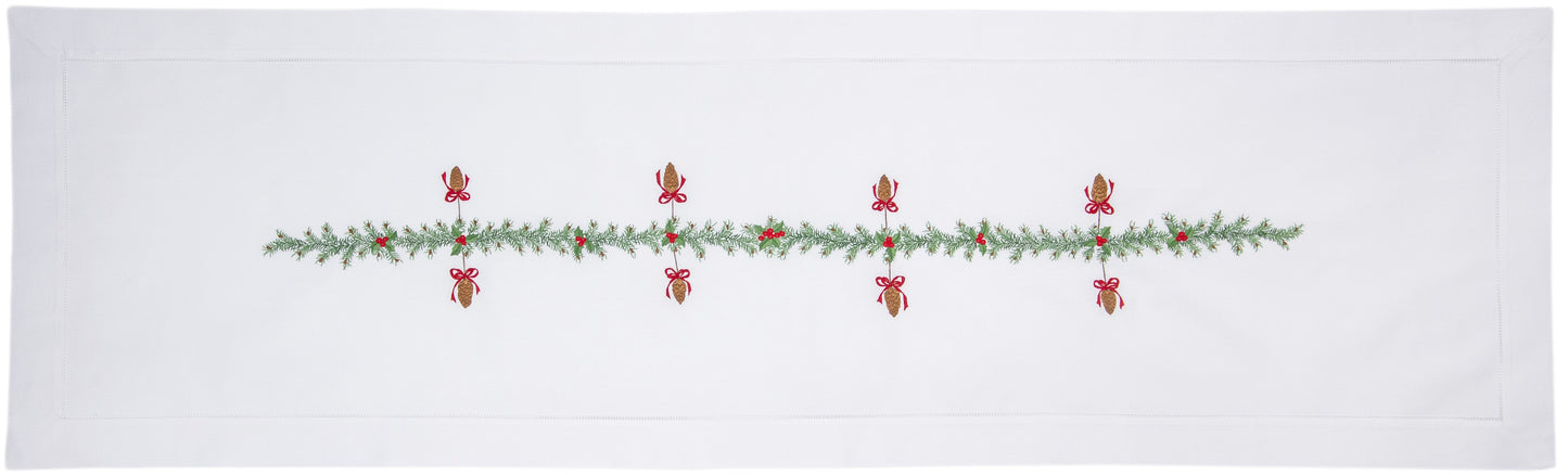 A white table runner with a hemstitch border. Pinecones extend in a line down the middle.