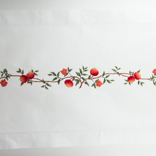 A white table runner with a hemstitch border. A branch of pomegranates extends down a line in the middle.