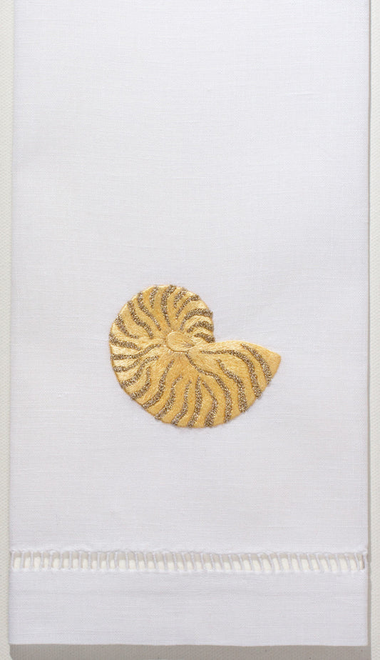 A white hand towel with a hemstitch. A gold nautilus shell is embroidered in the center
