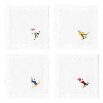 4 white cocktail napkins with a hemstitch border. Embroidered on the bottom right corner of each is a different skier