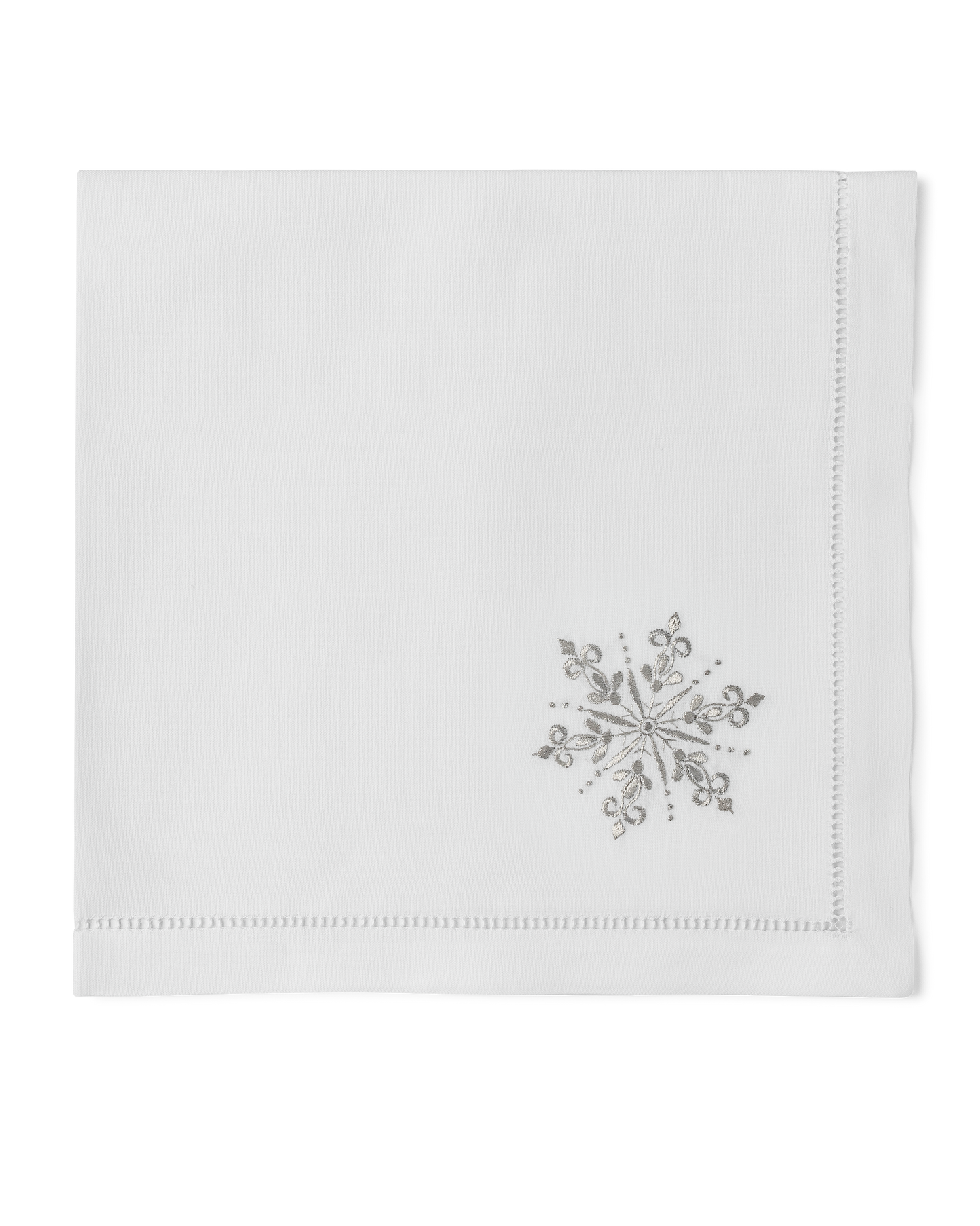 A white napkin with a hemstitch. A silver snowflake is embroidered in the bottom right corner