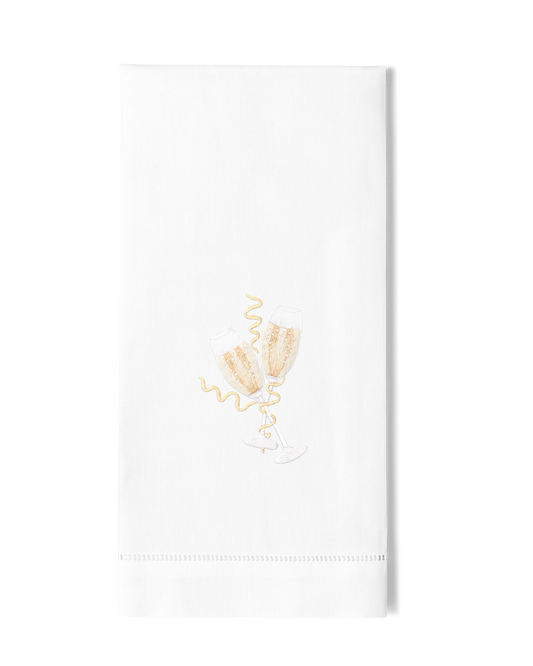 A white hand towel with a hemstitch. Two toasting champagne glasses are embroidered in the center.