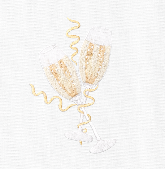A close up detailed image of the embroidery - Two filled champagne glasses toasting with gold bands wrapped around them.