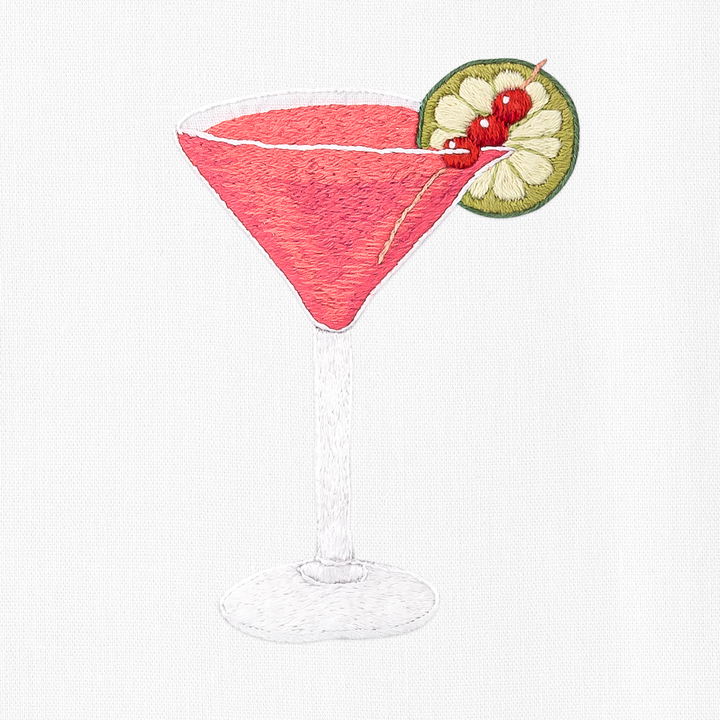 an embroidered cosmopolitan cocktail with a lime slice and cherries