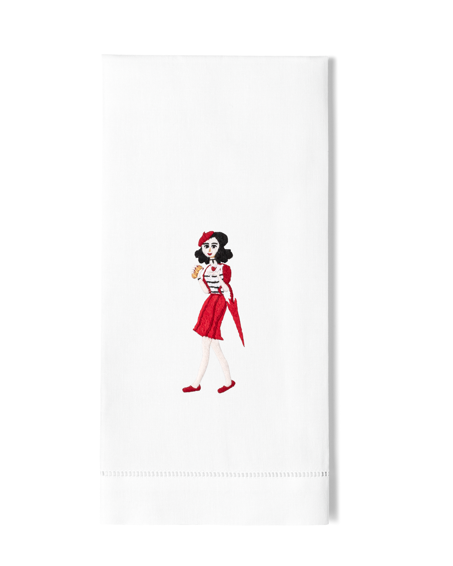 A white hand towel with a hemstitch. A woman in red holding a pastry is embroidered in the center.